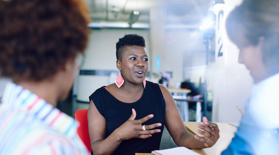 Black woman in an office setting talking with two other colleagues