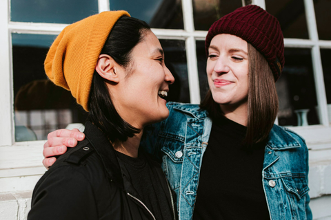 Two young women wearing beanie hats. One with their arm round the other, smiling and laughing with each other