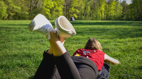 young woman laying on the grass at a park wearing red top and black jeans
