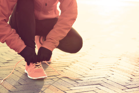 Female jogger lacing up her trainers before a run wearing pink trainers and top